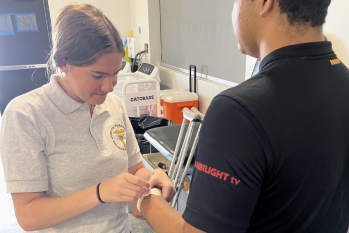 PHOTO: SPHS sports medicine student Keira Adams helps prepare football player Guillermo Melara for practice. (Photo Courtesy of Andre Zumaeta)
