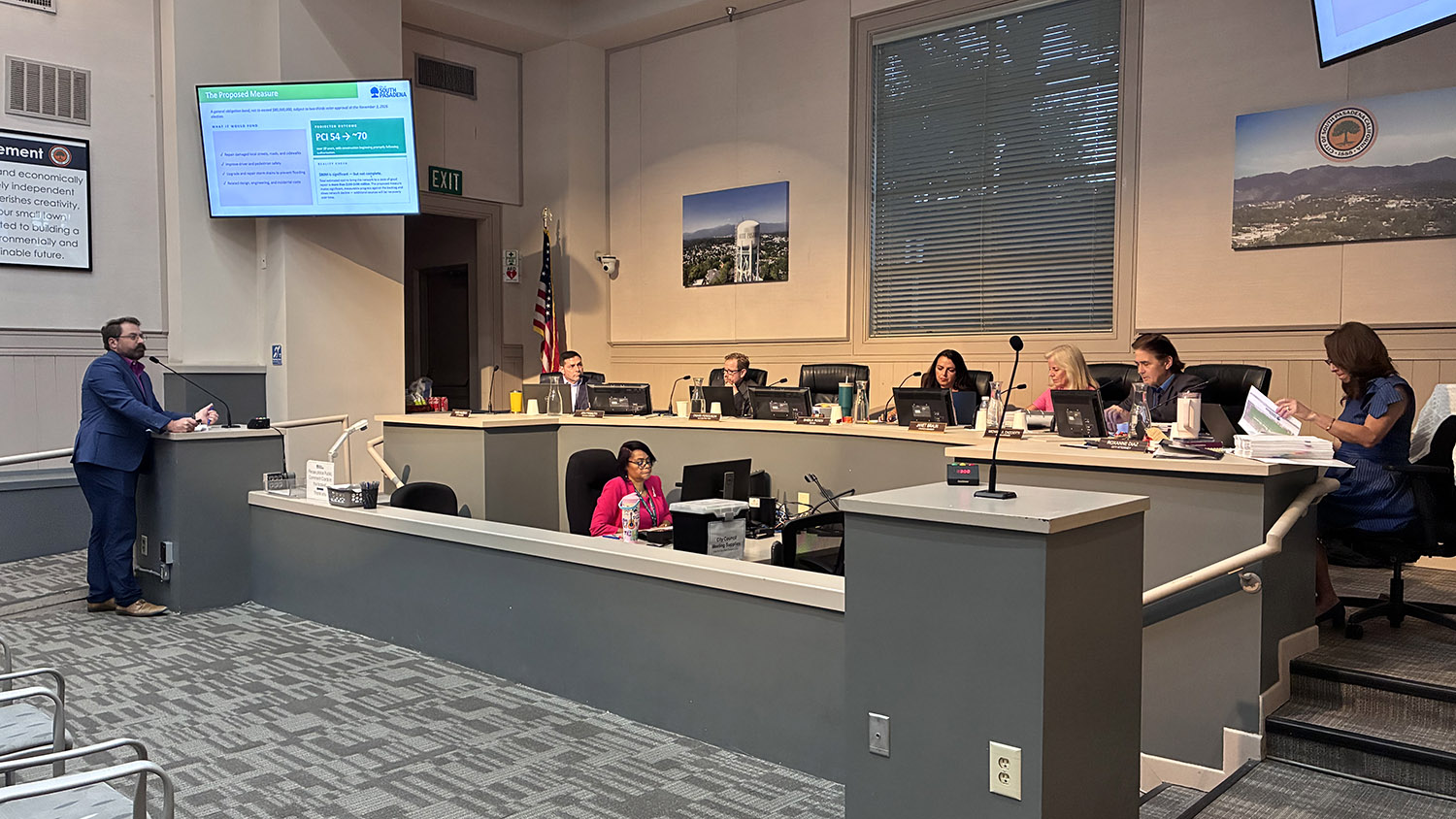 South Pasadena Finance Director, in a blue suit, speaks at a podium in a council chamber while officials sit at a curved desk with laptops and microphones behind him.