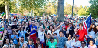 South Pasadena World Cup in Garfield Park crowd at a park celebration, many people raising hands and smiling, with an American flag visible in the background.
