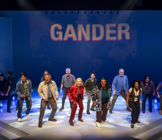 COME FROM AWAY soars on joy, hope and the kindness of strangers at A Noise Within Diverse cast dancing on a stage beneath a blue backdrop that reads GANDER.