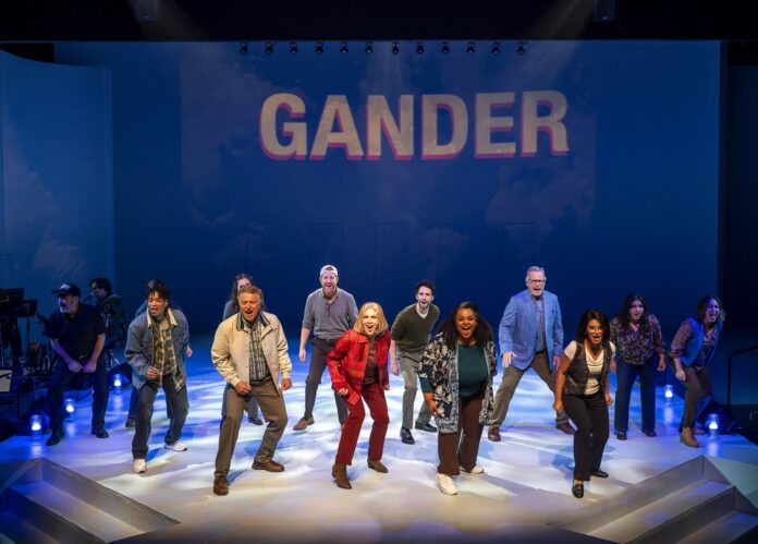 Diverse cast dancing on a stage beneath a blue backdrop that reads GANDER.