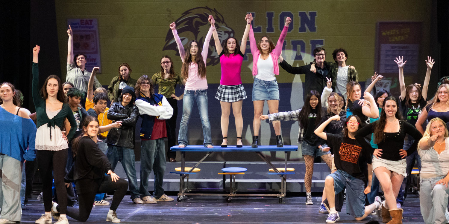| The South Pasadenan | South Pasadena News Group of students on a theater stage posing with arms raised, some standing on a blue riser while others stand or kneel around, suggesting a school performance or choir finale.