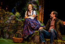 Betsy Morgan as Fiona and Max von Essen as Tommy in Brigadoon at Pasadena Playhouse. A Couple sits on a green hillside in the Scottish highlands. The man looks lovingly at the woman.