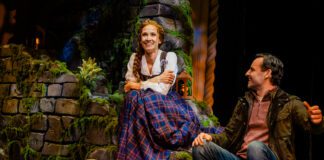 Betsy Morgan as Fiona and Max von Essen as Tommy in Brigadoon at Pasadena Playhouse. A Couple sits on a green hillside in the Scottish highlands. The man looks lovingly at the woman.