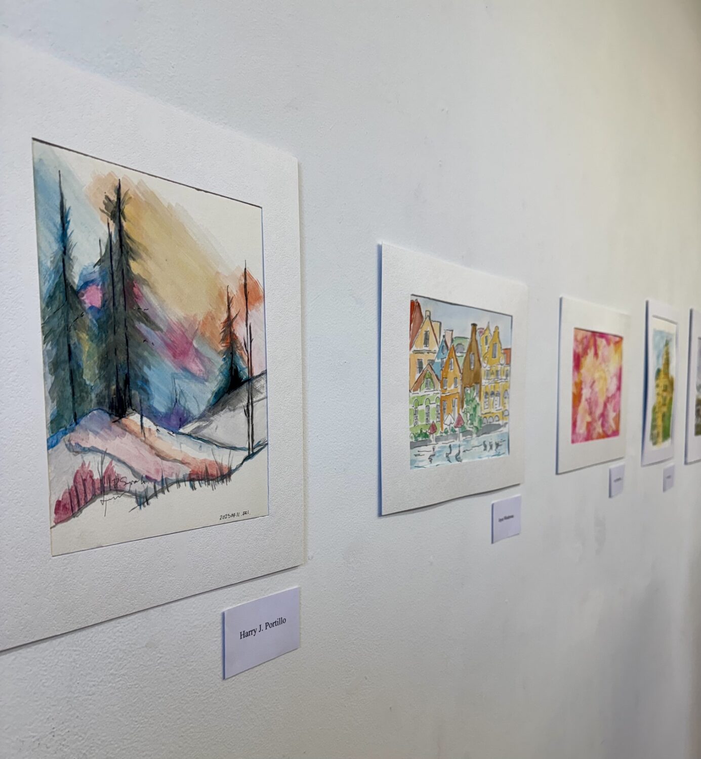 | The South Pasadenan | South Pasadena News Row of colorful watercolor paintings in white frames hung along a light gallery wall, the first piece depicting a snowy landscape with tall trees and vibrant sky hues