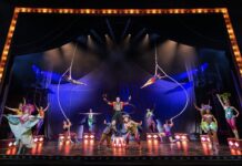 Water for Elephants – The Broadway Musical | Now Playing at Hollywood Pantages Circus stage with colorful performers; two aerialists swing from hoops above a central troupe under bright spotlights.
